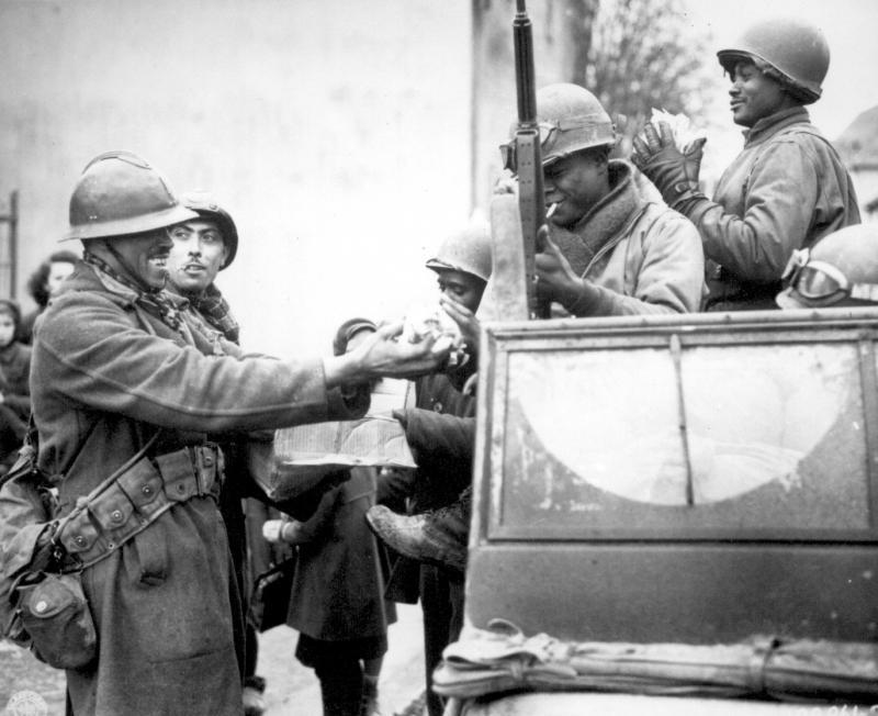 Two smiling French soldiers fill the hands of American soldiers with candy